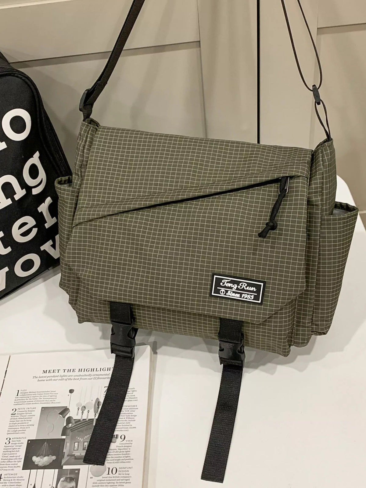 Front view of olive checked messenger bag with diagonal zip pocket and two black buckle closures