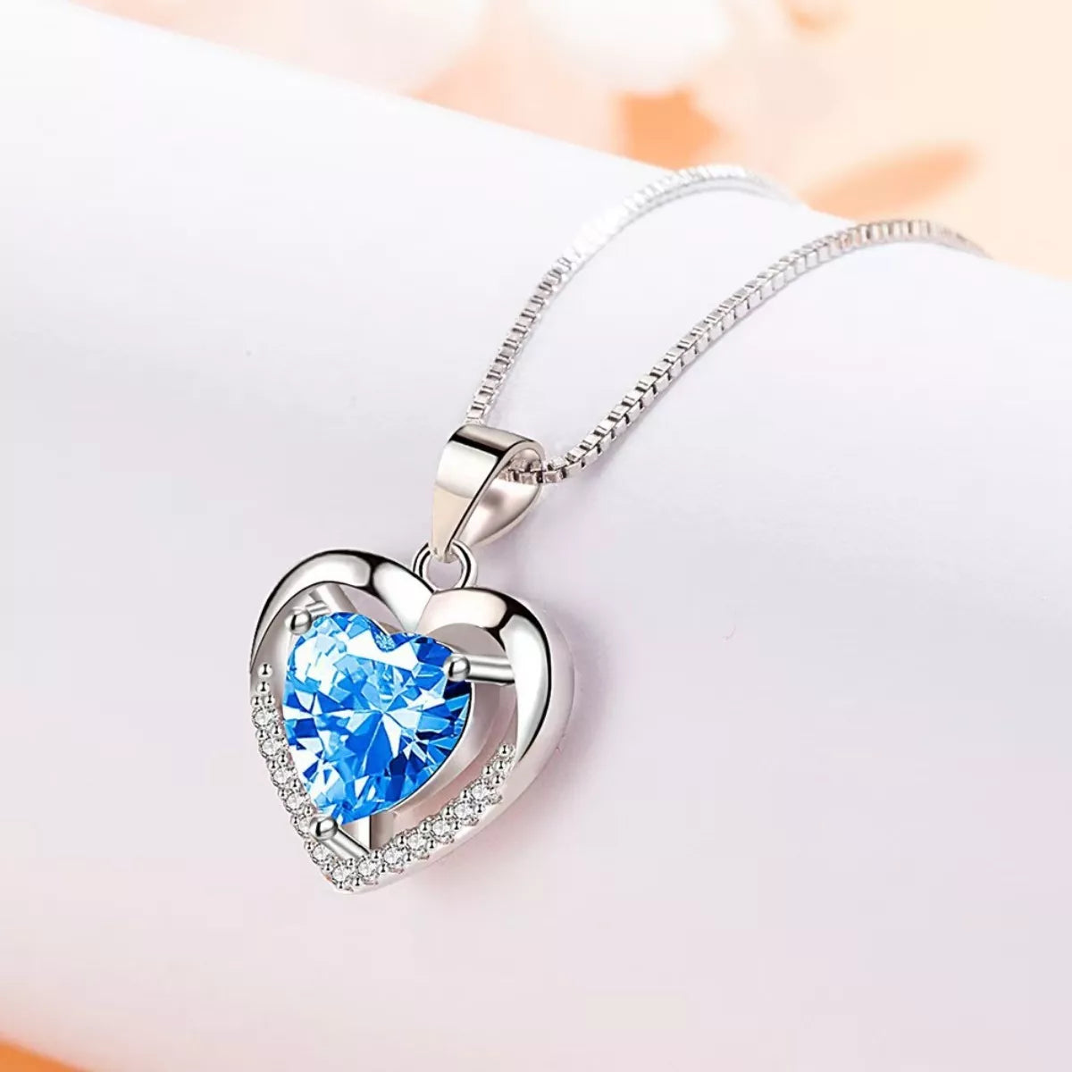 Silver-tone heart necklace with blue center stone on white background