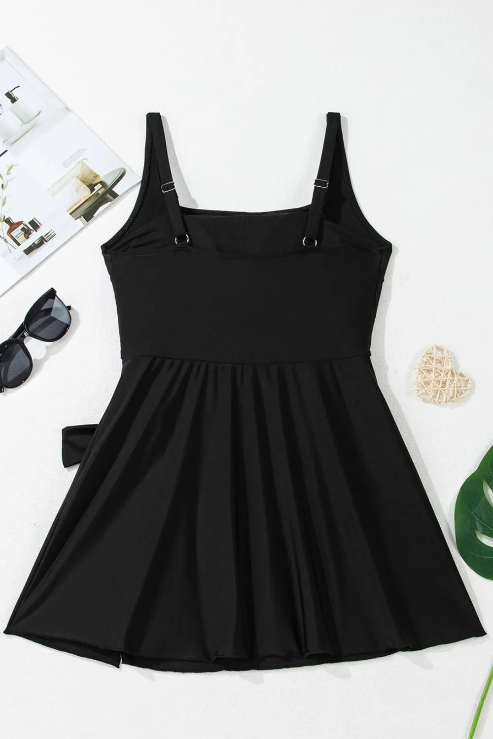 Flat lay of the black swim dress showing wide straps, gathered skirt and side ties.