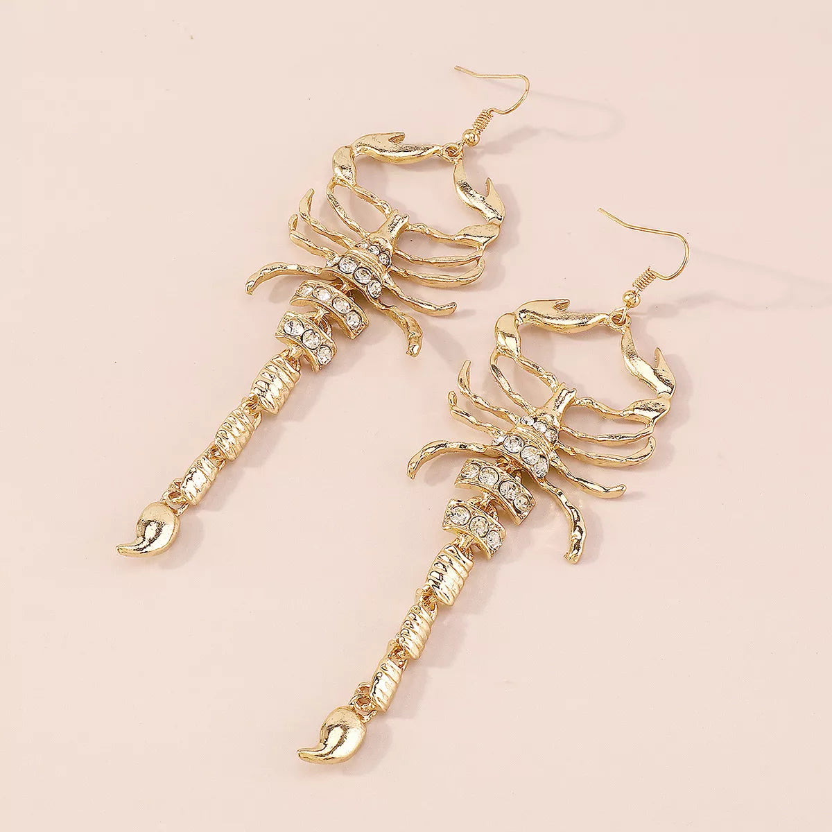 Pair of gold-tone scorpion earrings arranged diagonally on pale surface