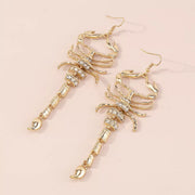 Pair of gold-tone scorpion earrings arranged diagonally on pale surface