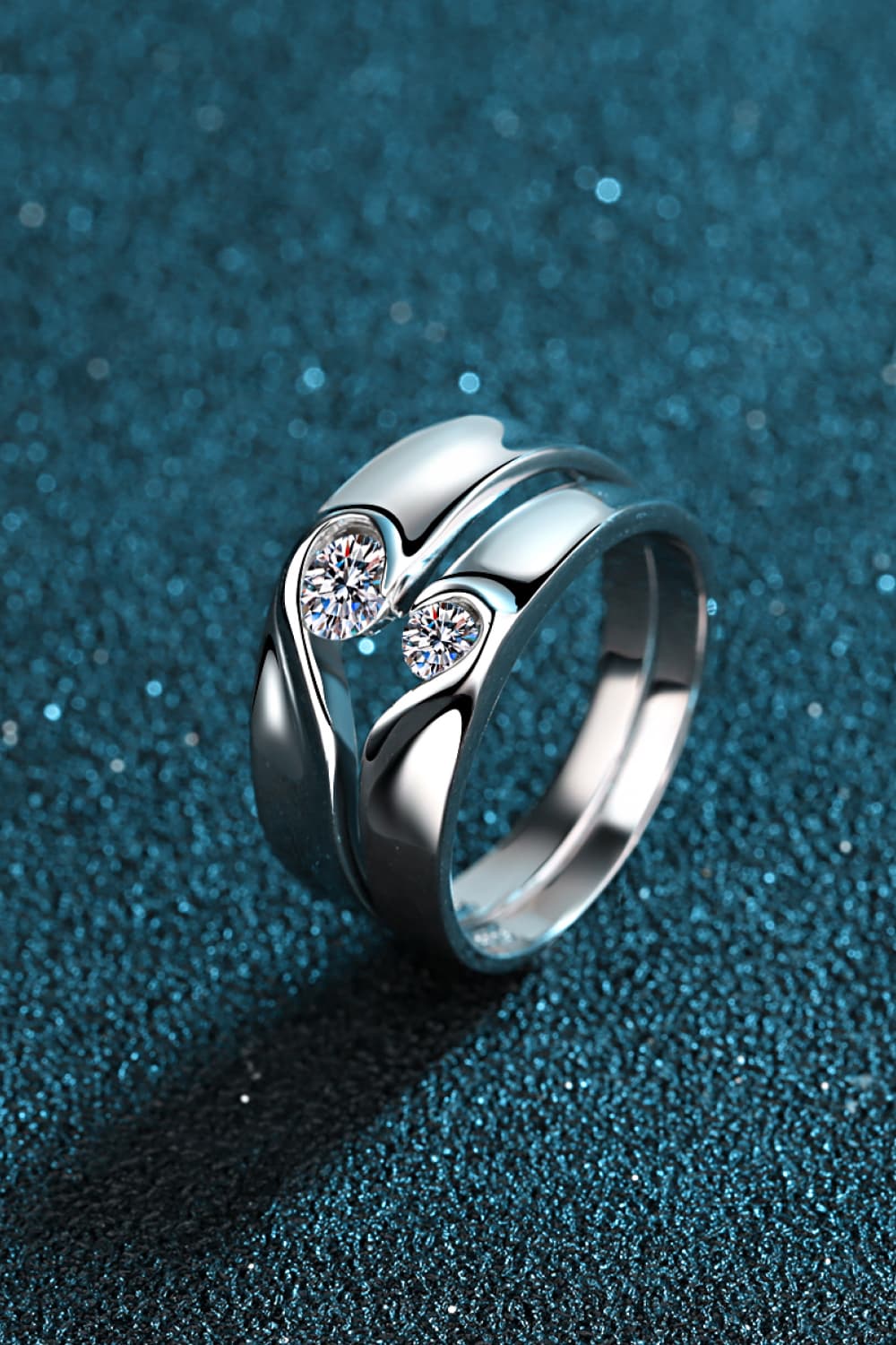 Angled view of a sculptural rhodium-plated ring with two moissanite stones on teal.
