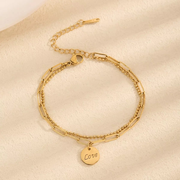 Gold-tone chain bracelet with round LOVE letter charm on a light surface