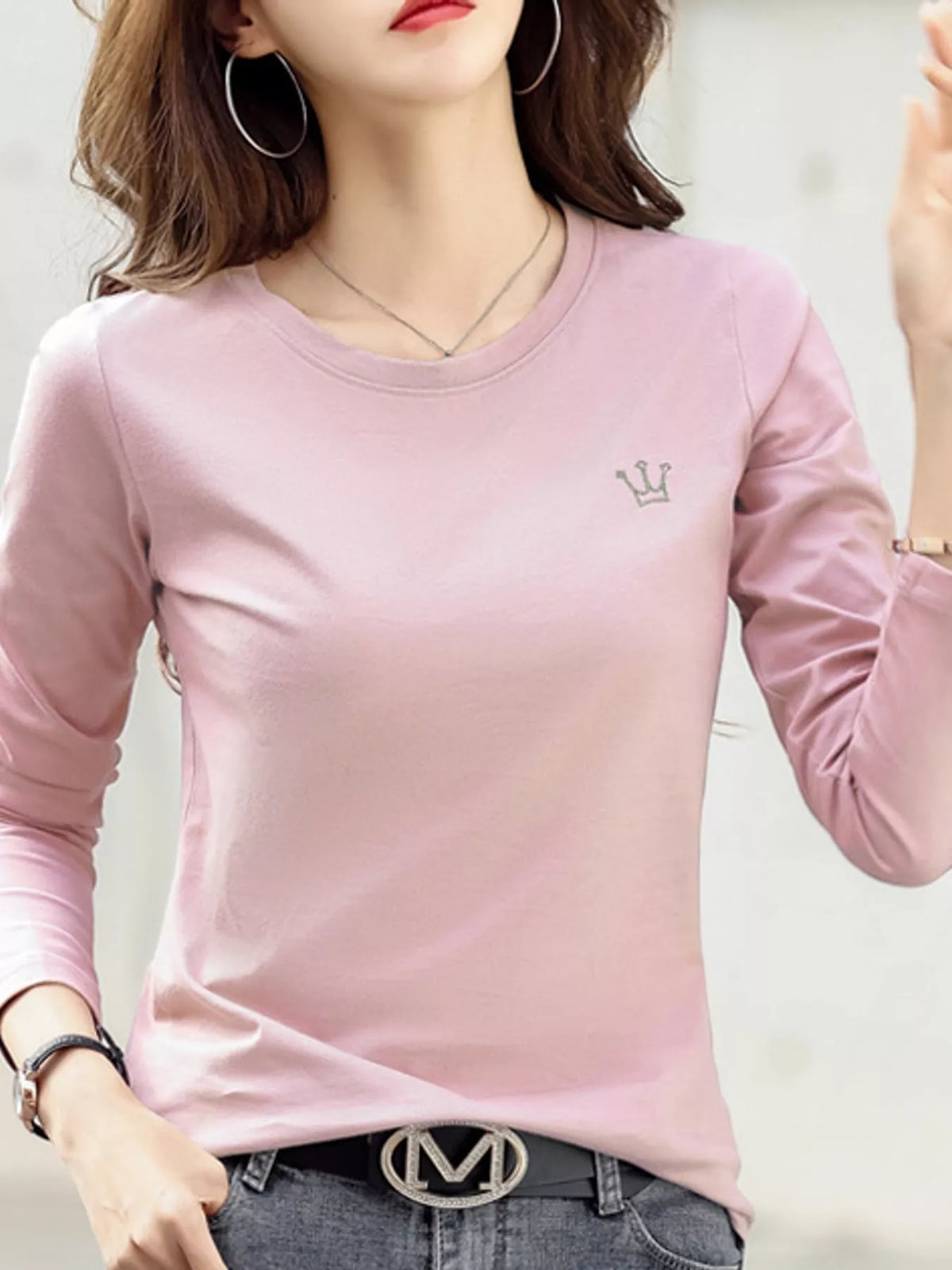 Pink long-sleeve T-shirt with small crown emblem, shown on a model from the front.