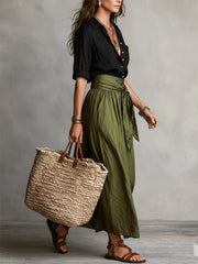 Side view of black shirt and olive green midi skirt with a woven tote bag.