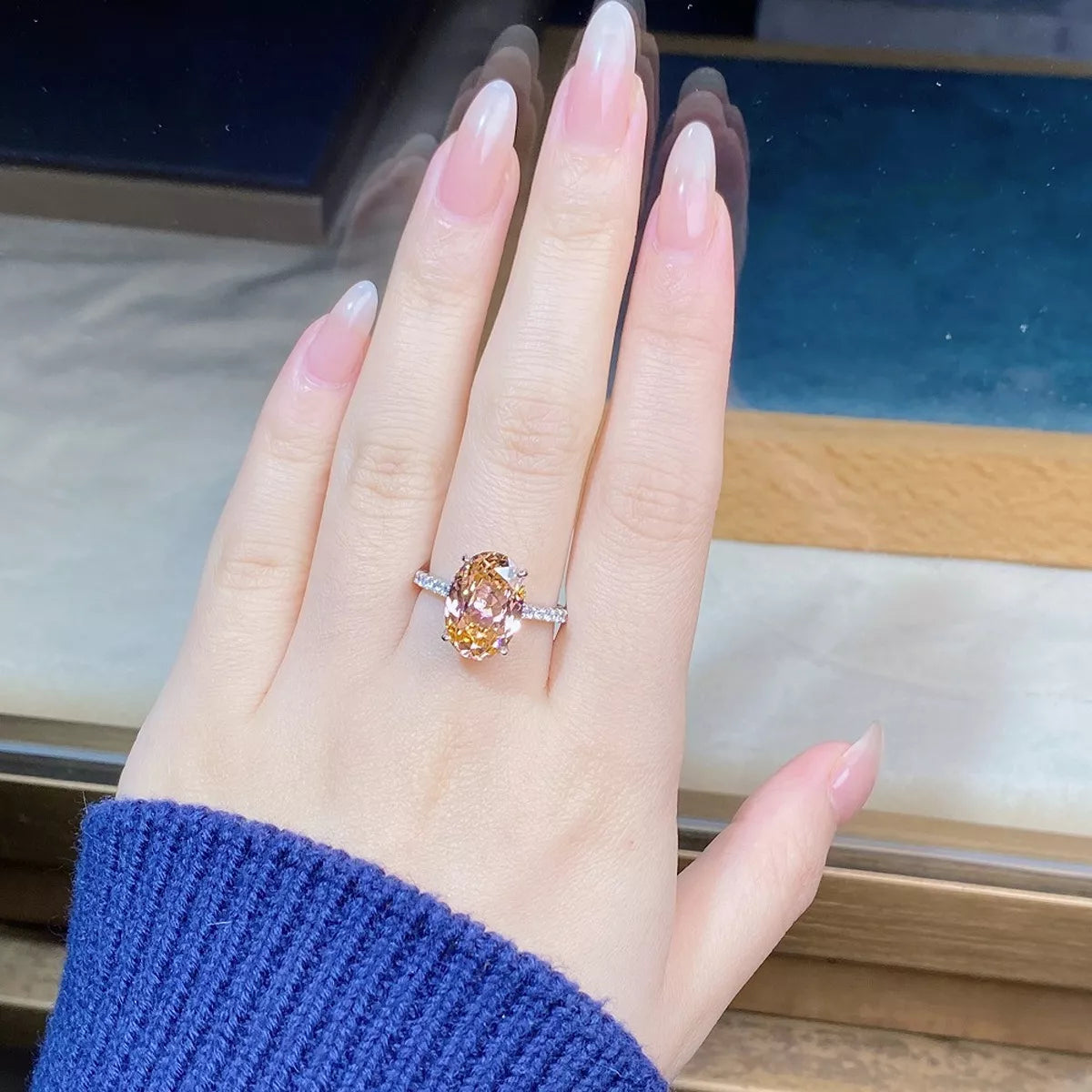 Oval watermelon-pink gemstone ring with clear shoulder stones worn on a hand