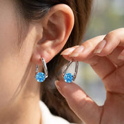 Gold-tone hoop earrings with blue round stones worn on an ear