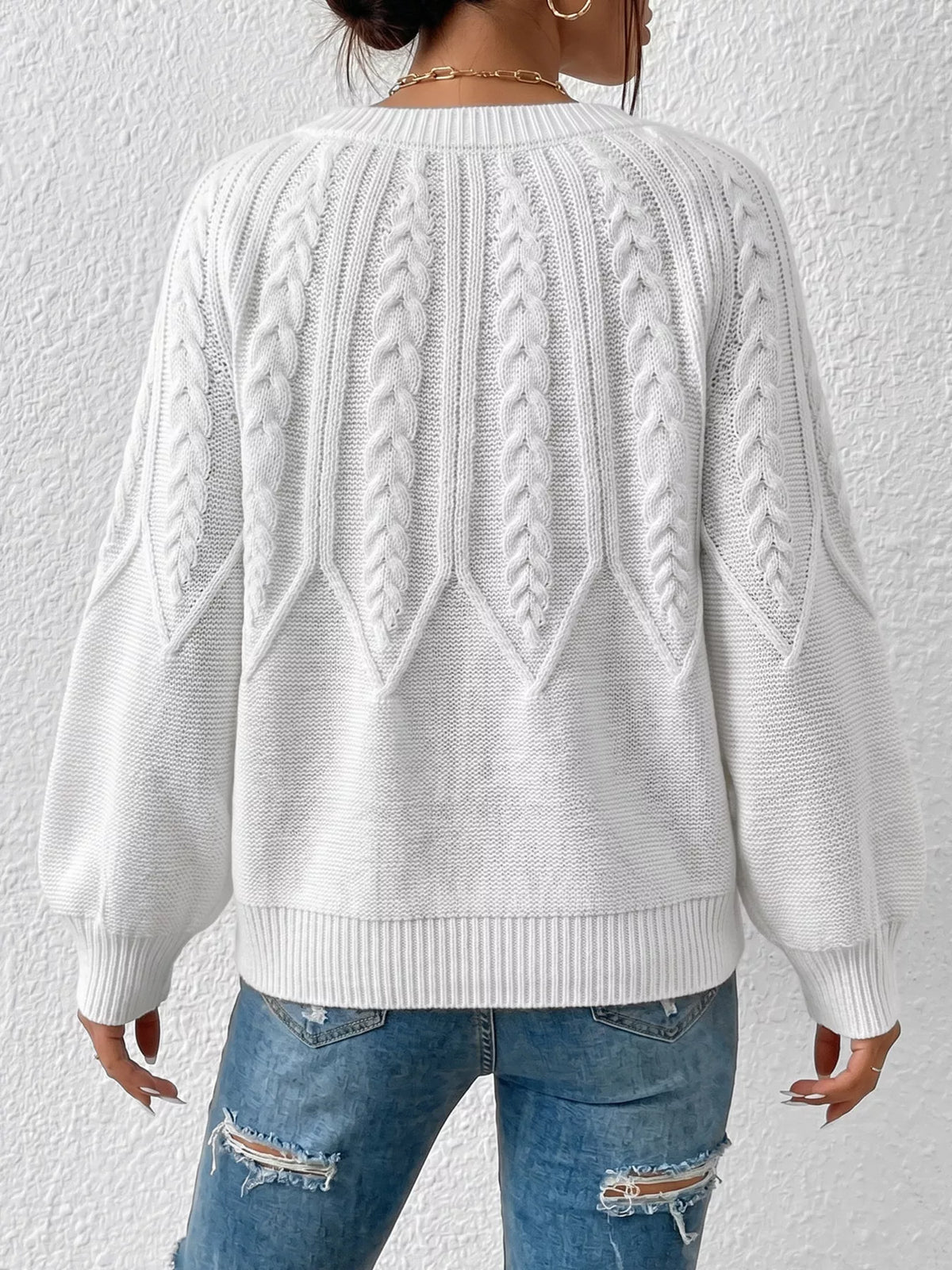 White cable-knit sweater shown from the back on a model