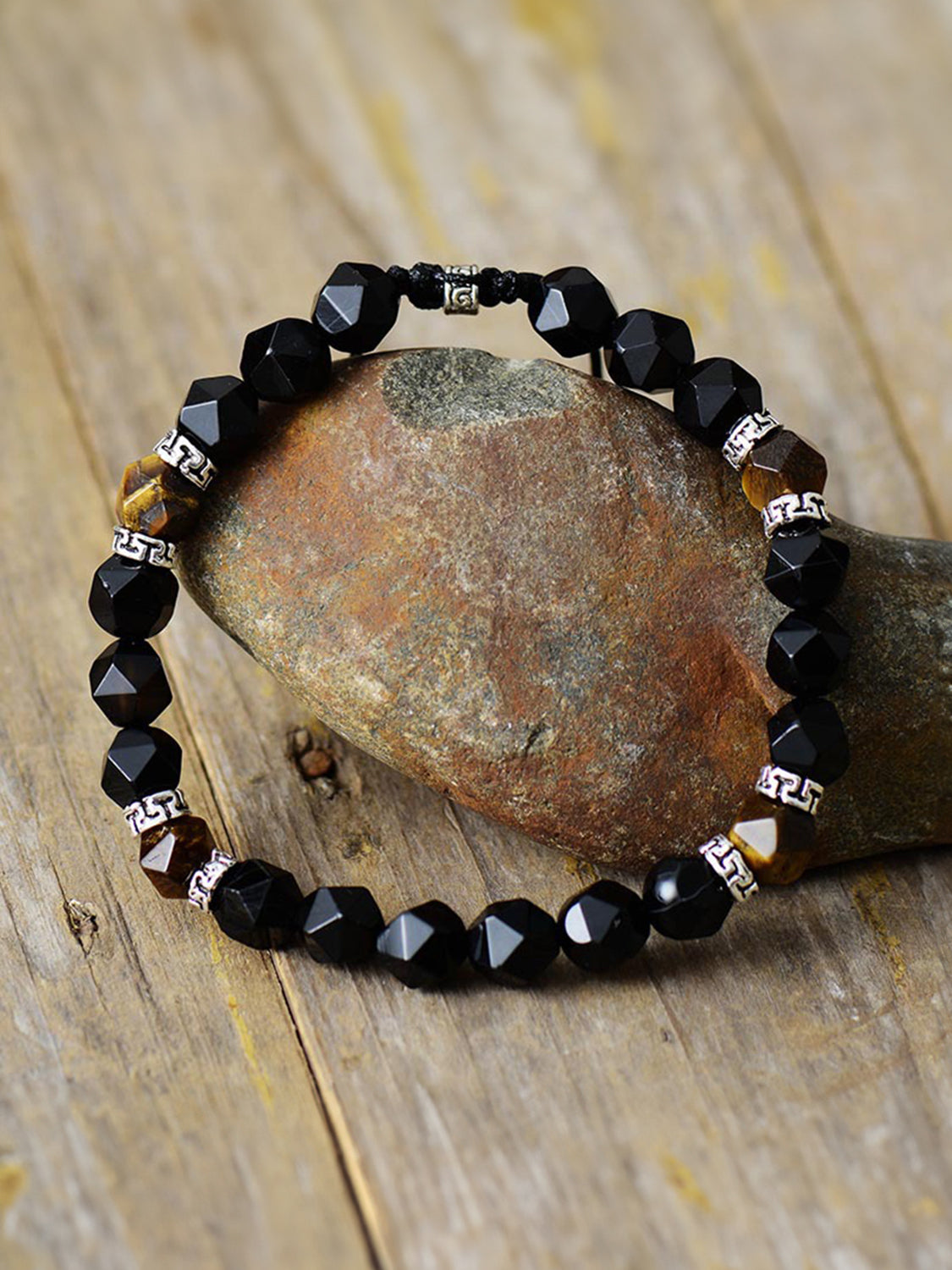 Black stone bracelet with a few brown accents displayed around a rock on wood