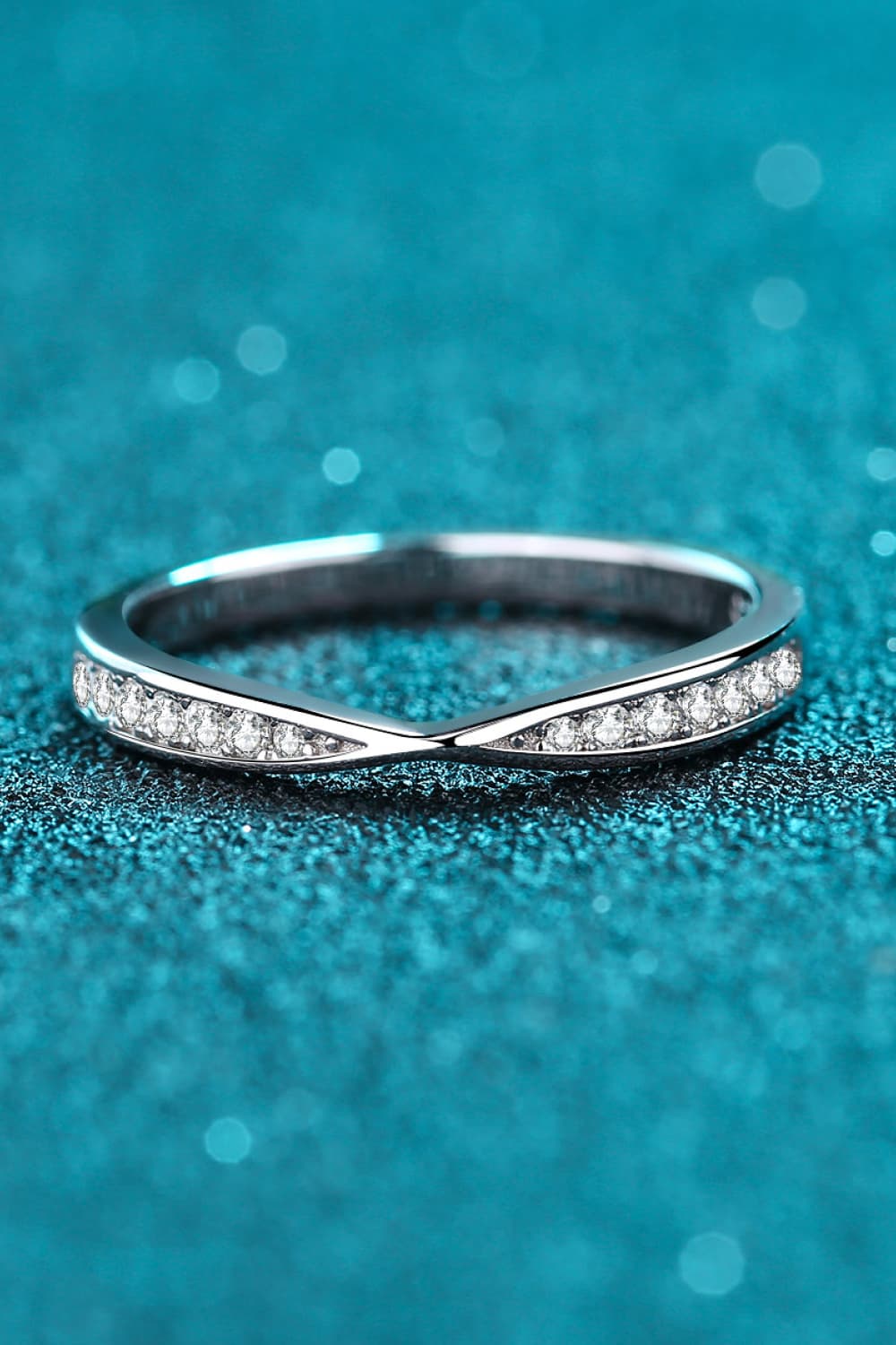 Low side view of a narrow pavé ring against teal.