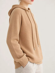 Light tan sweater shown at an angle with one hand in a white trouser pocket.