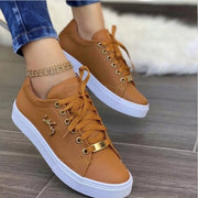 Brown lace-up sneakers with perforated panels and white soles worn with jeans