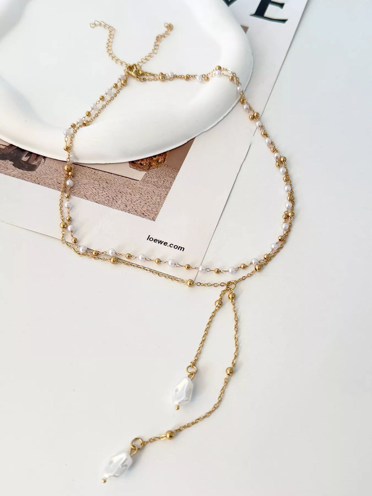 Gold-tone pearl Y necklace with two pendant drops displayed on a surface