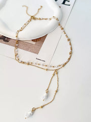Gold-tone pearl Y necklace with two pendant drops displayed on a surface