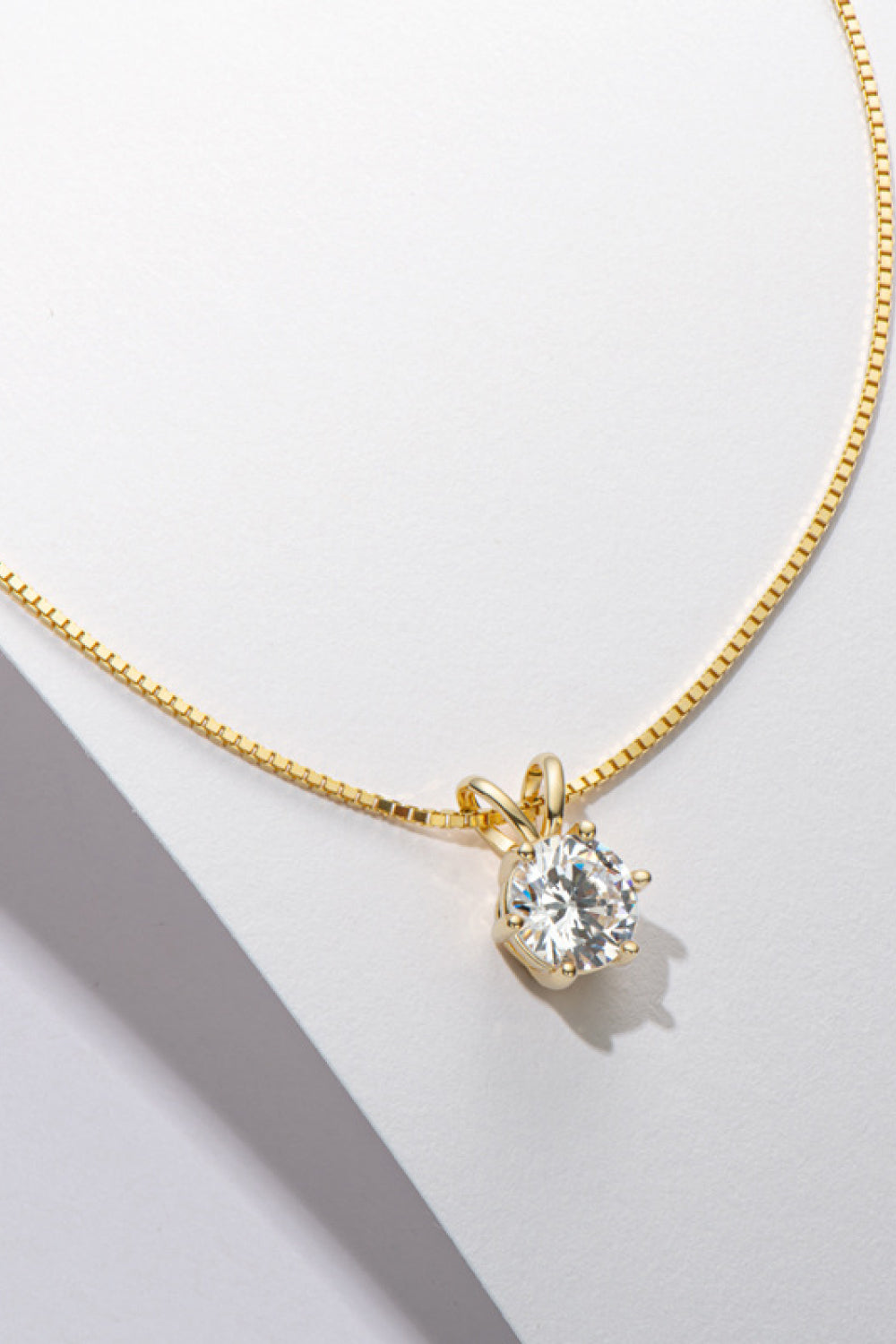 Gold-tone solitaire pendant necklace draped over a white display edge