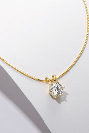 Gold-tone solitaire pendant necklace draped over a white display edge