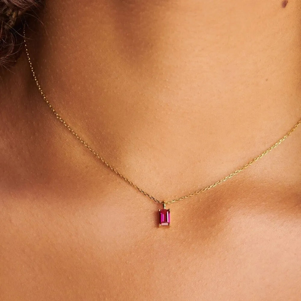 Red rectangular pendant on a fine gold-tone chain at the neckline
