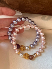 Two pearl-bead bracelets with gold filigree balls and red, mauve and crystal accents held in a hand