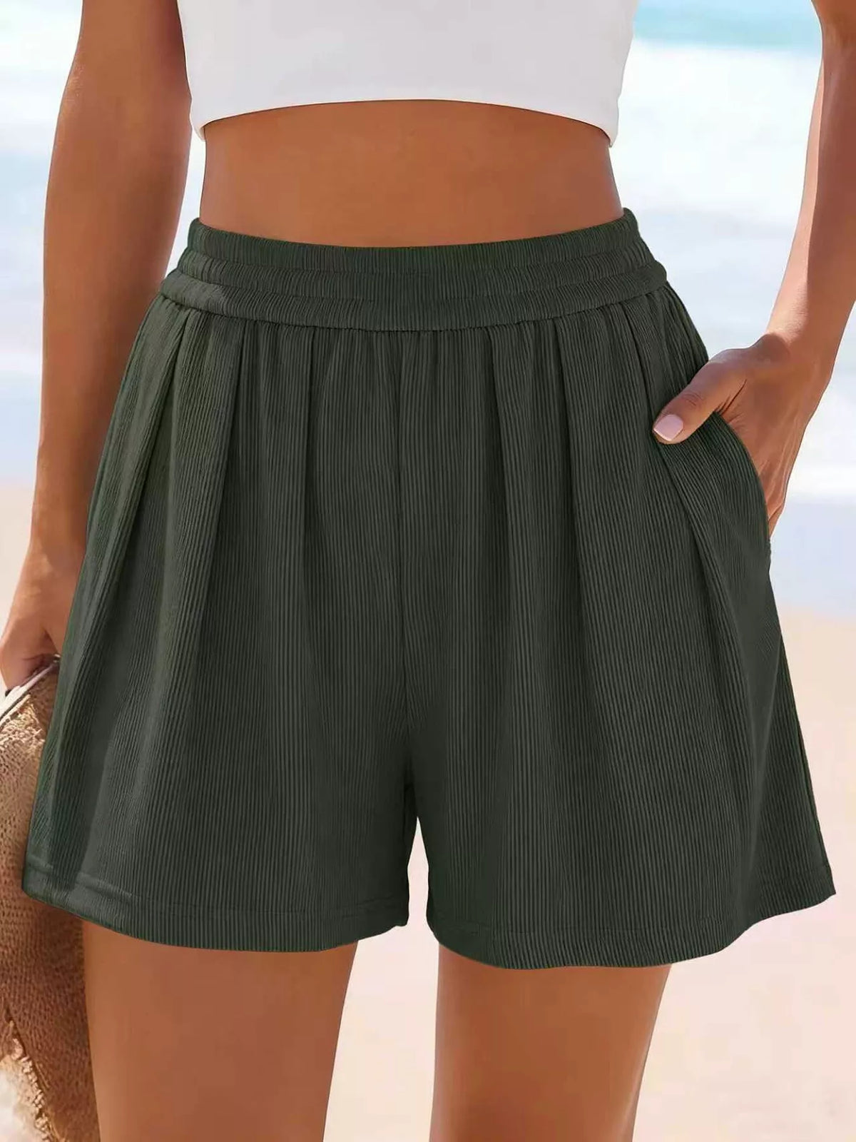 Front view of dark green shorts with hand at the waist