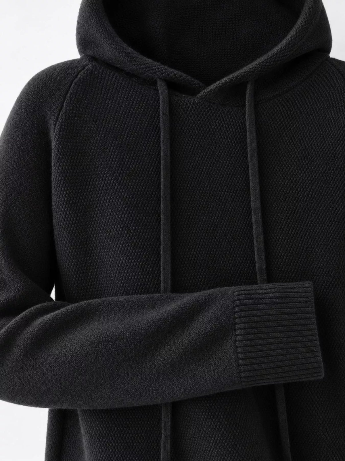 Black sweater close-up showing the hood, drawstrings, textured knit and ribbed cuff.