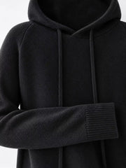 Black sweater close-up showing the hood, drawstrings, textured knit and ribbed cuff.
