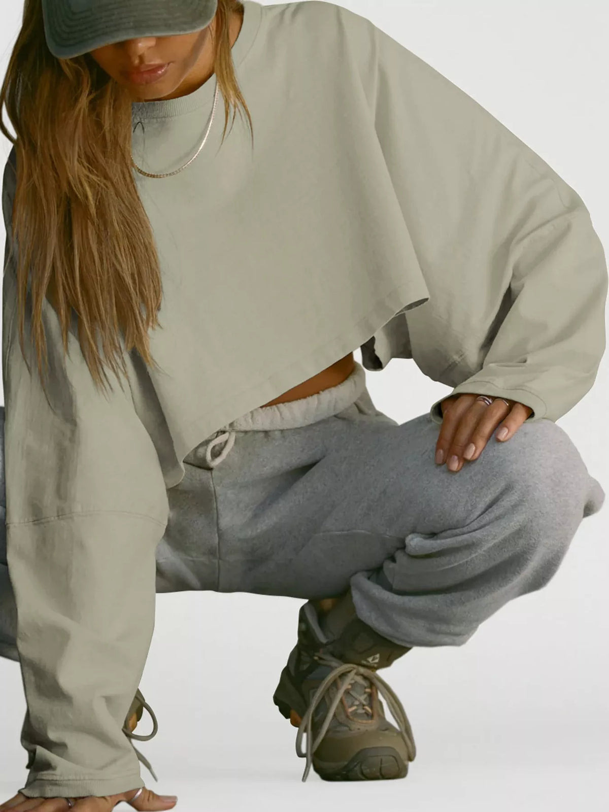 A model crouches in a pale sage cropped sweatshirt and gray sweatpants.