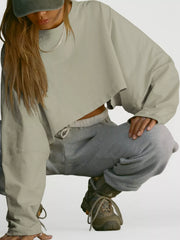 A model crouches in a pale sage cropped sweatshirt and gray sweatpants.