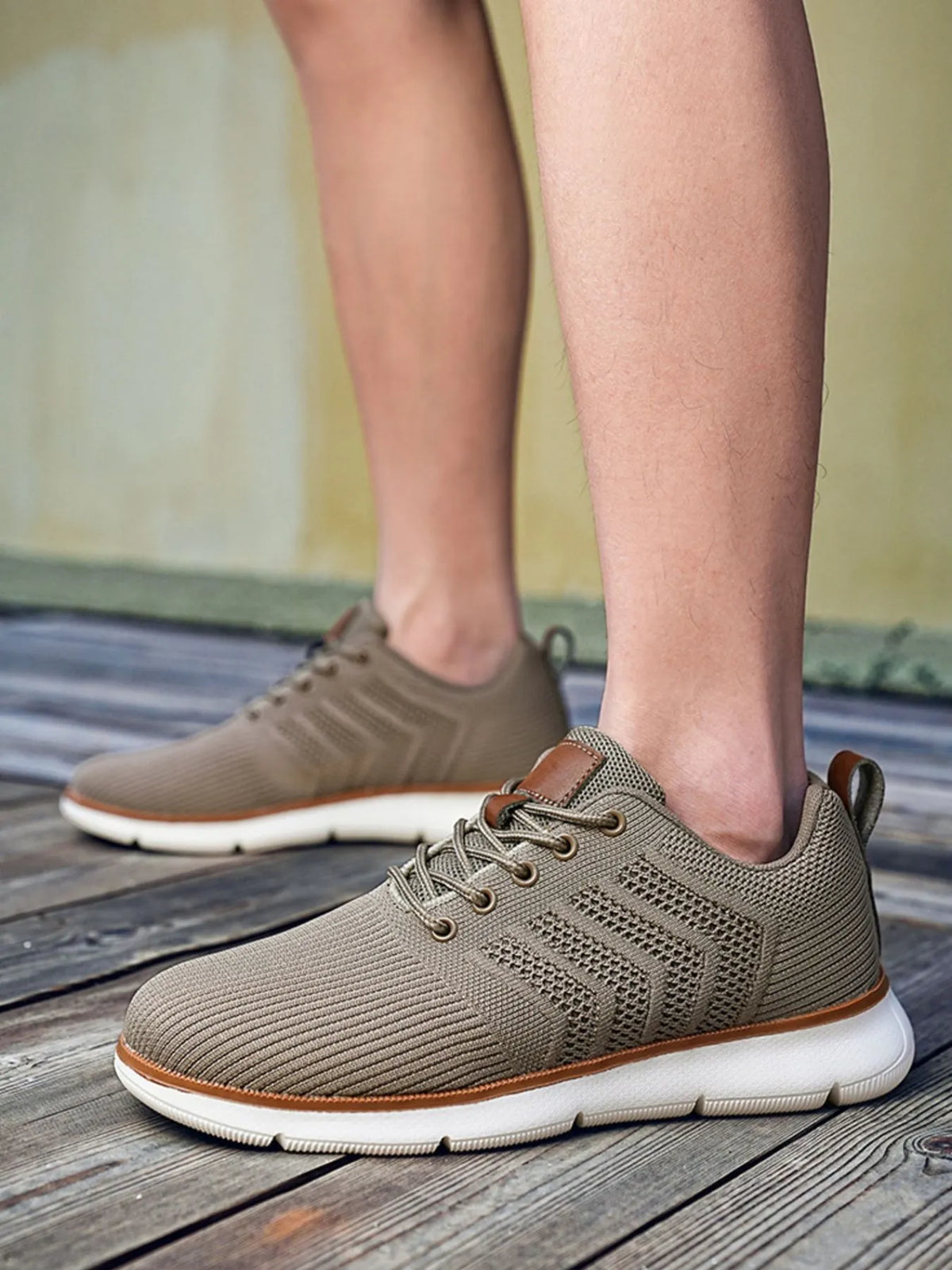 Taupe knit lace-up shoes with brown trim, worn on a wooden deck