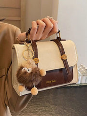 Close view of cream and brown flap bag with decorative charm and top handle
