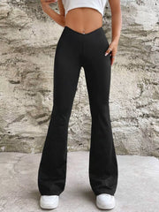 Black flared pants with a V-shaped waistband, front view with one hand at the hip against a stone wall.