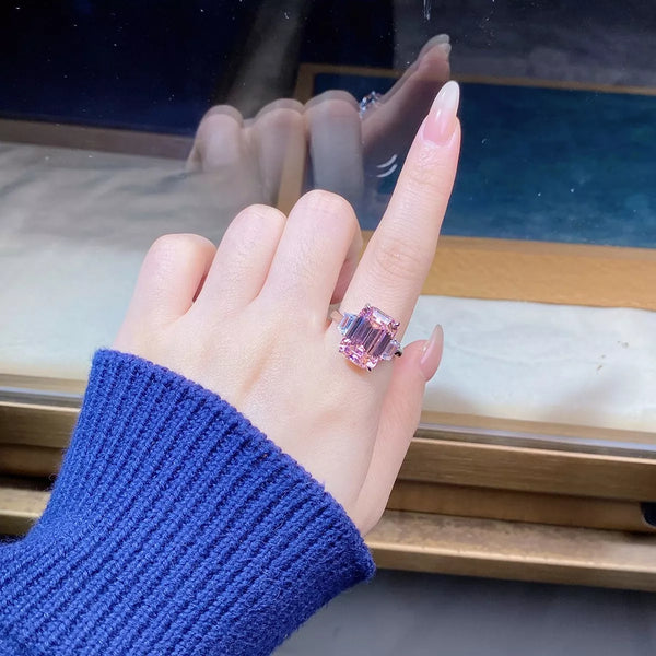 Rectangular pink geometric gemstone ring with clear side stones worn on a hand