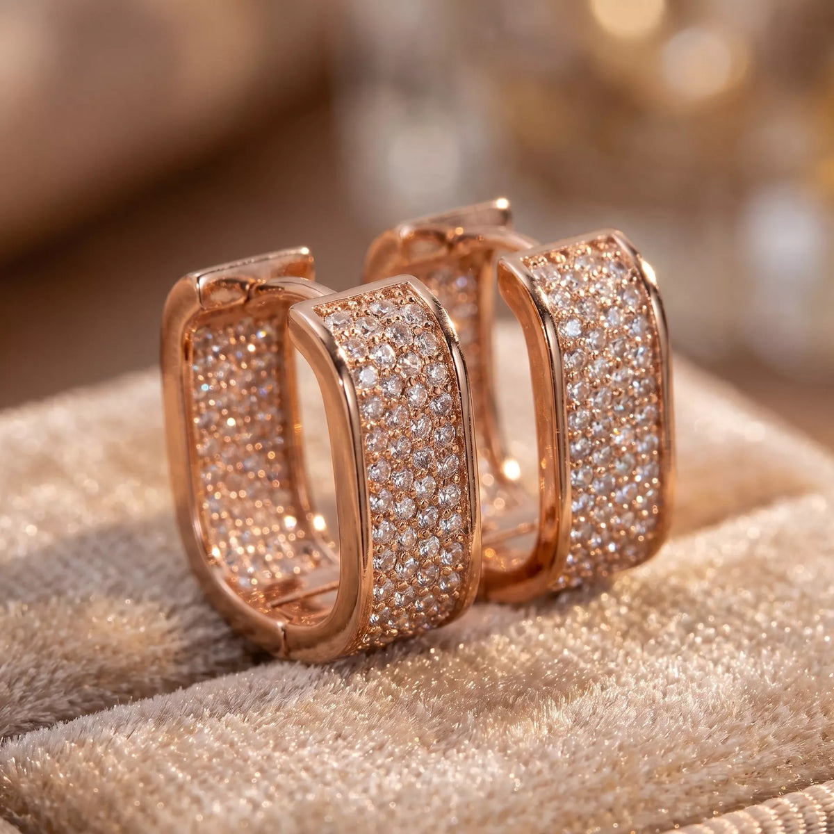 Rose-gold-tone square hoop earrings with clear stones on pale fabric