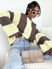 Model leaning in cream and brown oversized sweater, showing wide striped sleeves