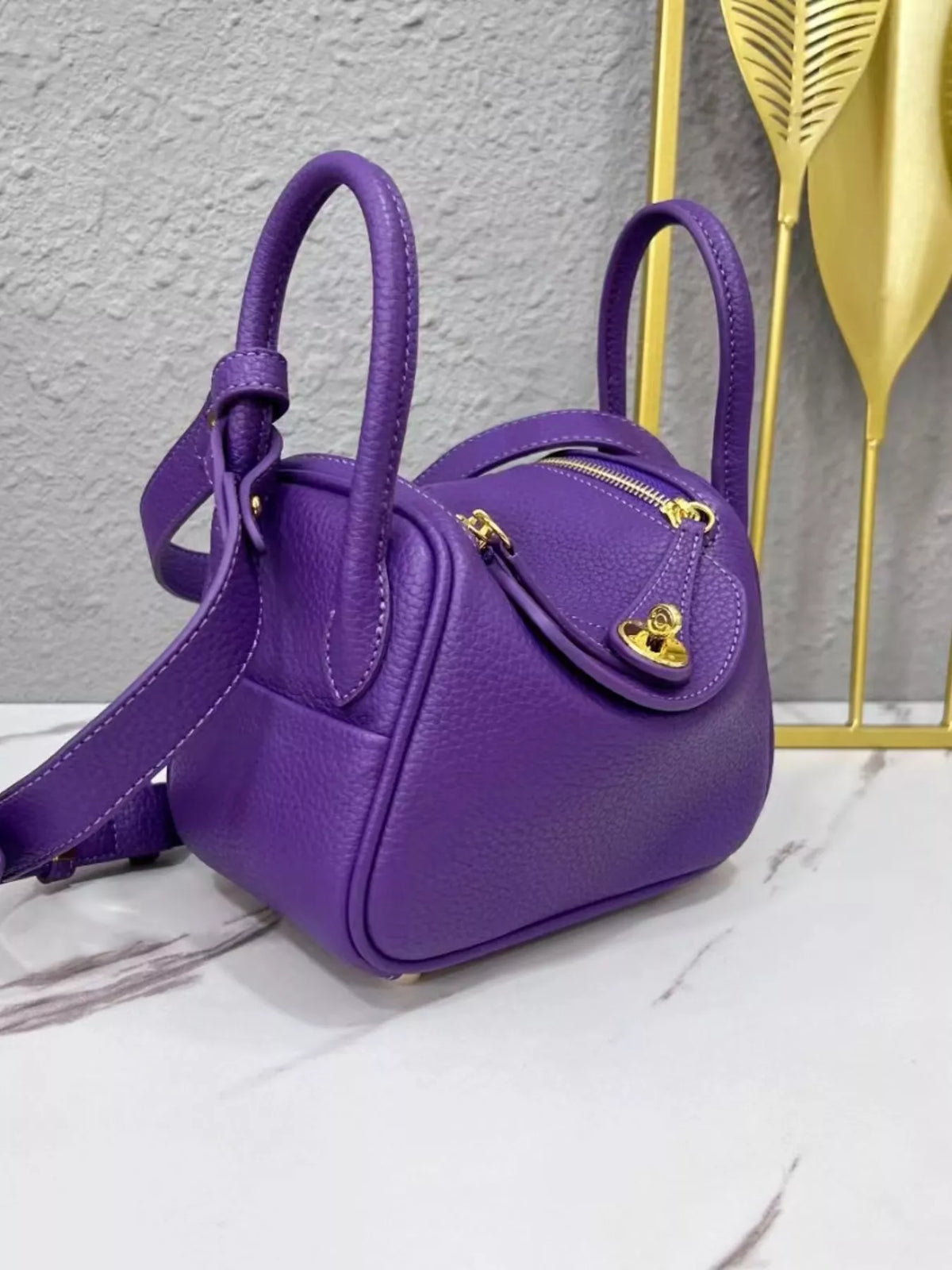 Three-quarter view of a purple crossbody bag with gold-tone hardware
