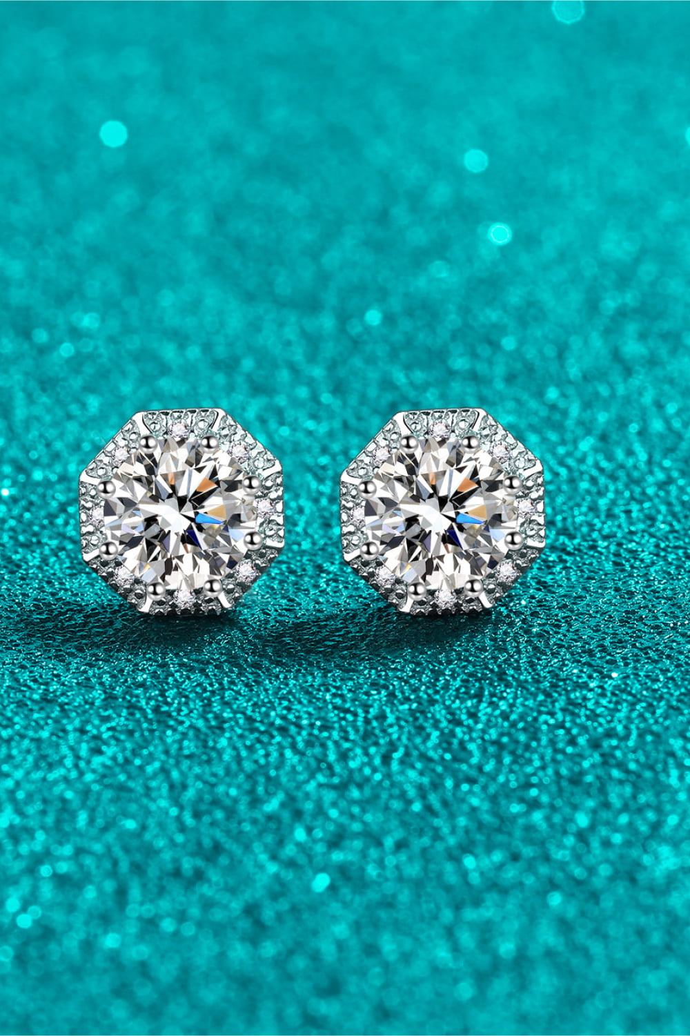 Pair of round moissanite studs displayed on teal background