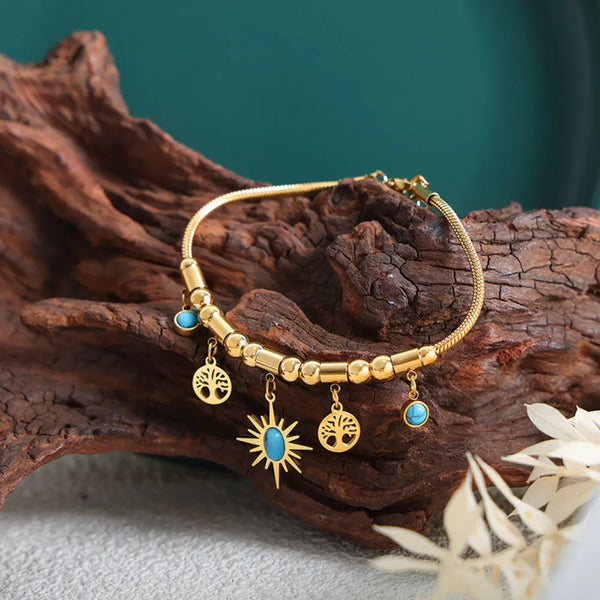 Gold charm bracelet with blue stones and sun pendant on driftwood