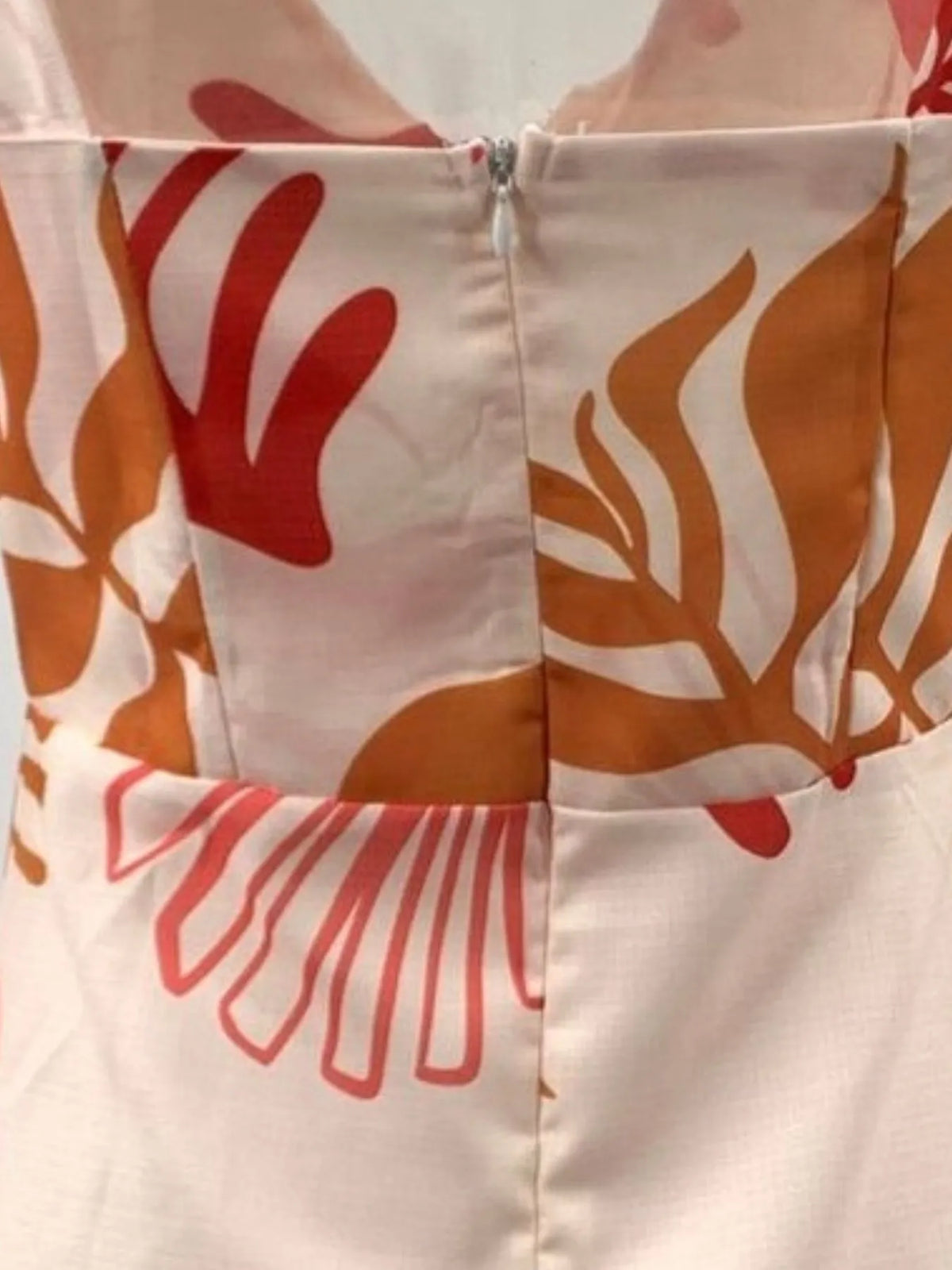 Close view of coral, rust and beige leaf print on the light dress fabric.