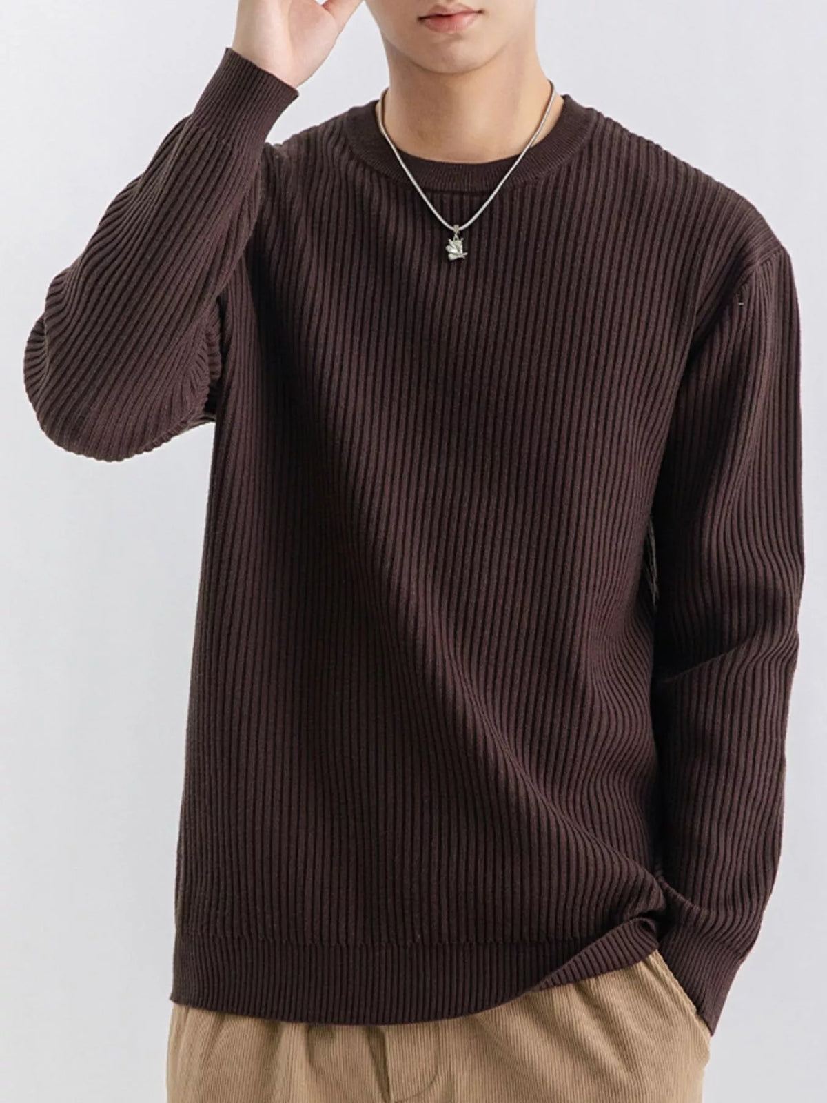 Model wearing a dark brown ribbed sweater with one hand raised beside the head