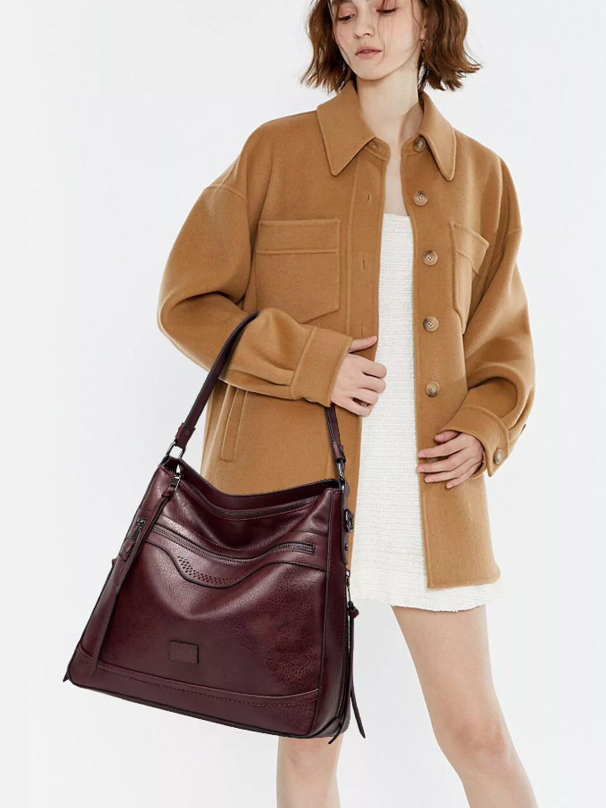 Burgundy multi-pocket handbag carried at the side by a model