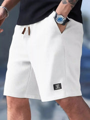 Model wearing white waffle-textured drawstring shorts with side pockets and a small hem label