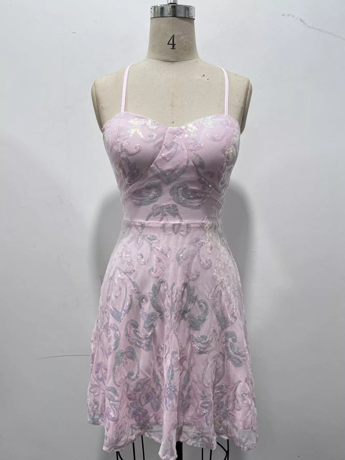 Pale lilac floral-sequin mini dress displayed on a dress form against a wall.