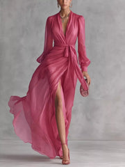 Pink long-sleeve wrap maxi dress with a tied waist and high slit, shown walking.