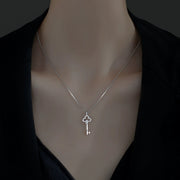 Model wearing a small key pendant necklace over a dark top