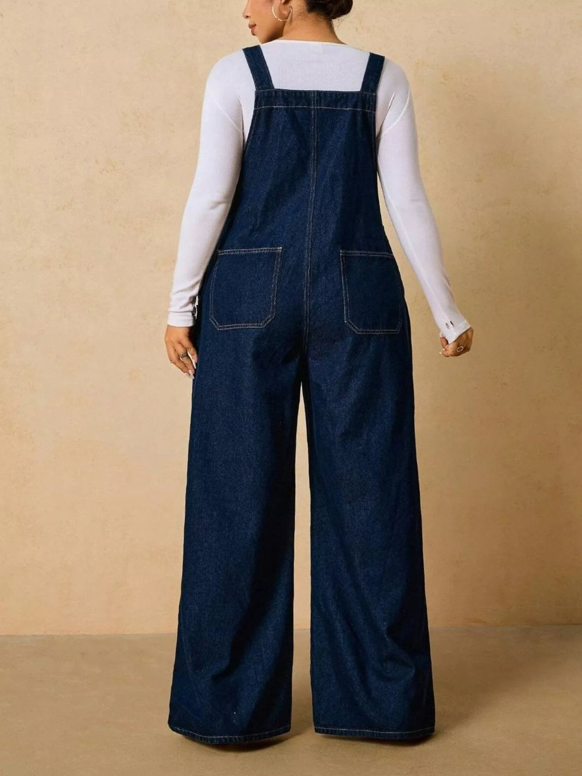 Back view of dark blue wide-leg overalls showing shoulder straps and two rear pockets.