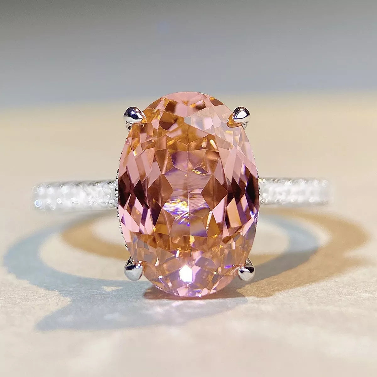 Front close-up of a faceted oval pink gemstone held by silver-tone prongs