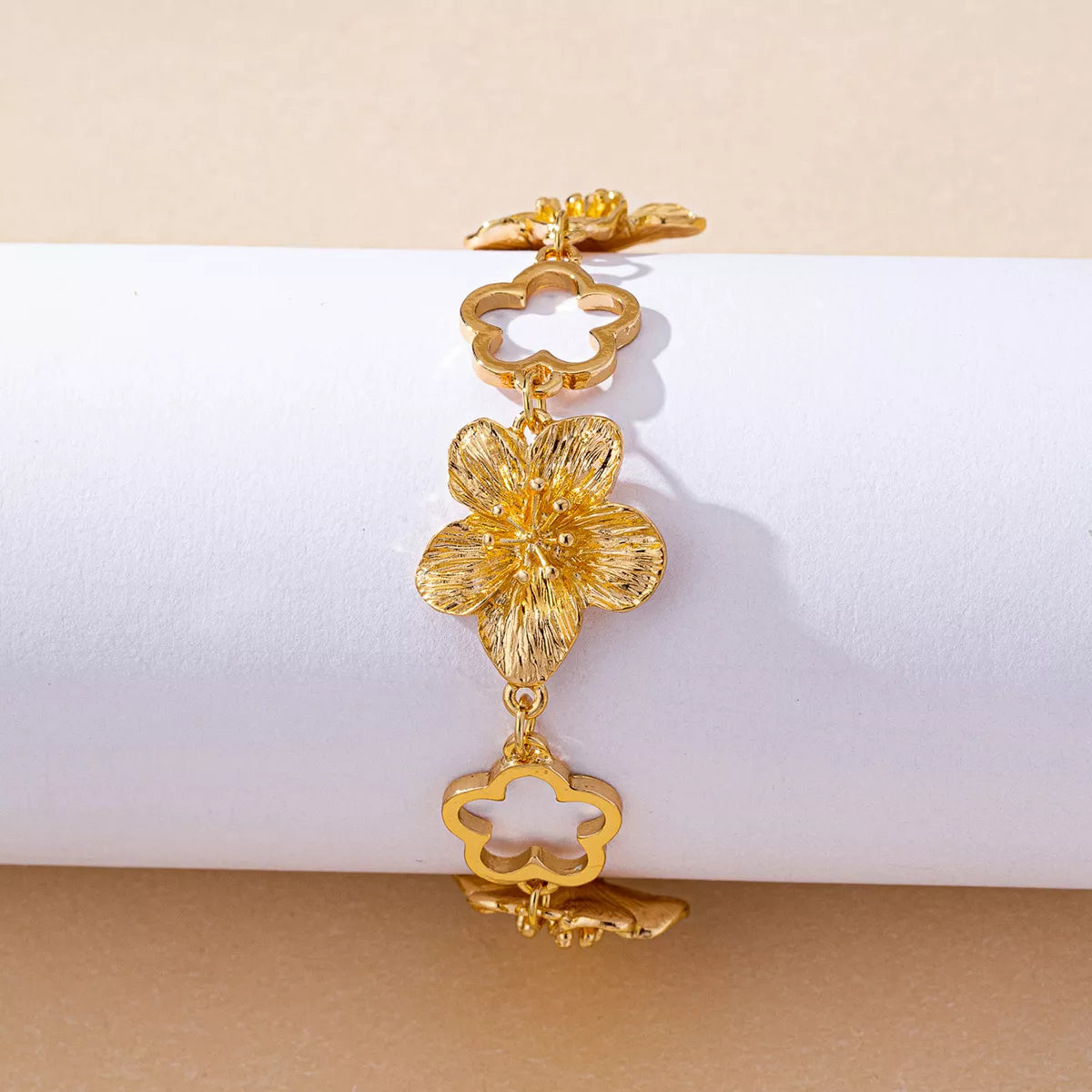 Gold-tone flower bracelet arranged vertically on a display block