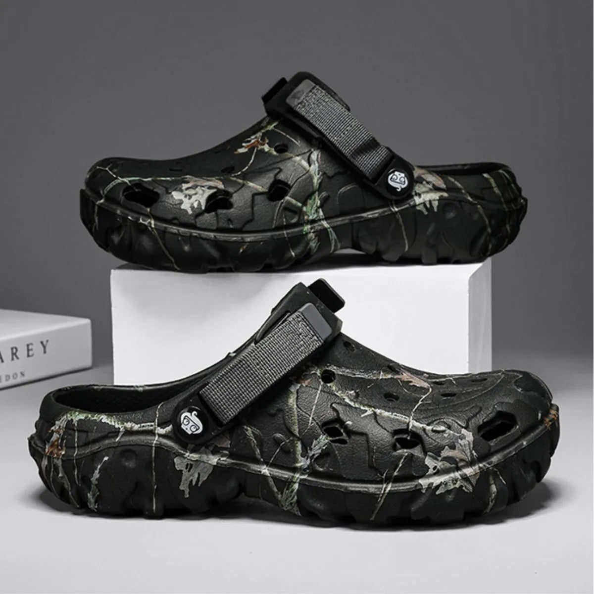 Pair of black branch-print clogs displayed on white blocks