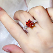 Three-carat red-orange moissanite ring with clear side stones worn on a hand