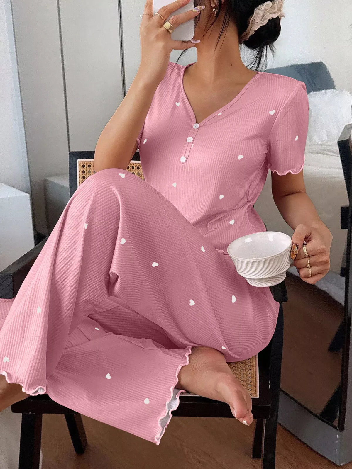 Seated model wearing pink heart-print loungewear set with lettuce-trim hems