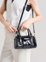 Black patent-look mini Boston crossbody bag held by its top handles, with the detachable strap visible.